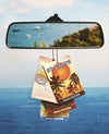 Car air freshener with St. Barts design hanging from a rearview mirror over water.