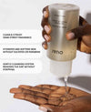 Hand holding a bottle of Ouidad product with text about its features on a white background