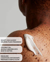 Close-up of a person's bare upper back and shoulder with a dollop of white cream applied to the skin. Text overlays describe the fragrance as velvety-rich and rosy melrose, mention coconut oil absorption, and name Squalane benefits.