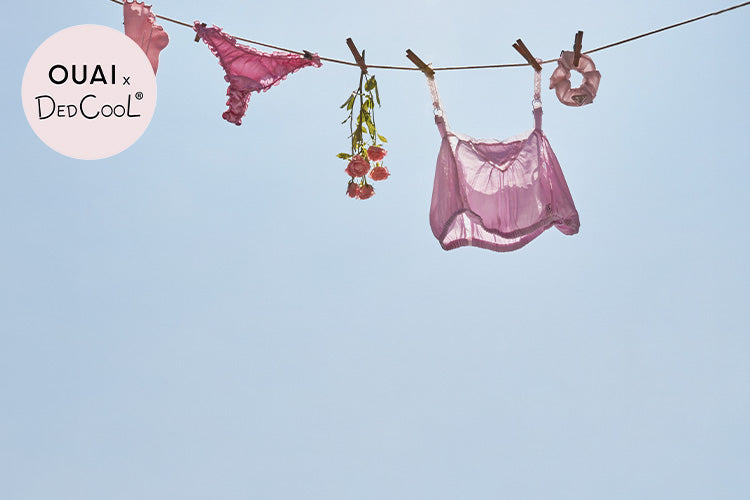 Pink lingerie and bralette hanging on a clothesline against a clear blue sky, with OUAI x DedCool logo.