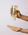 OUAI Fine Hair Shampoo dispensing from bottle into open palm, white background.