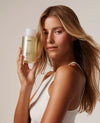 OUAI Fine Hair Shampoo held by blonde model in white top, neutral background.