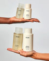 Hands holding OUAI hair care products against a light gray background