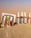 4 OUAI hair & body mist  deluxe size bottles standing on sand and on a sunset background