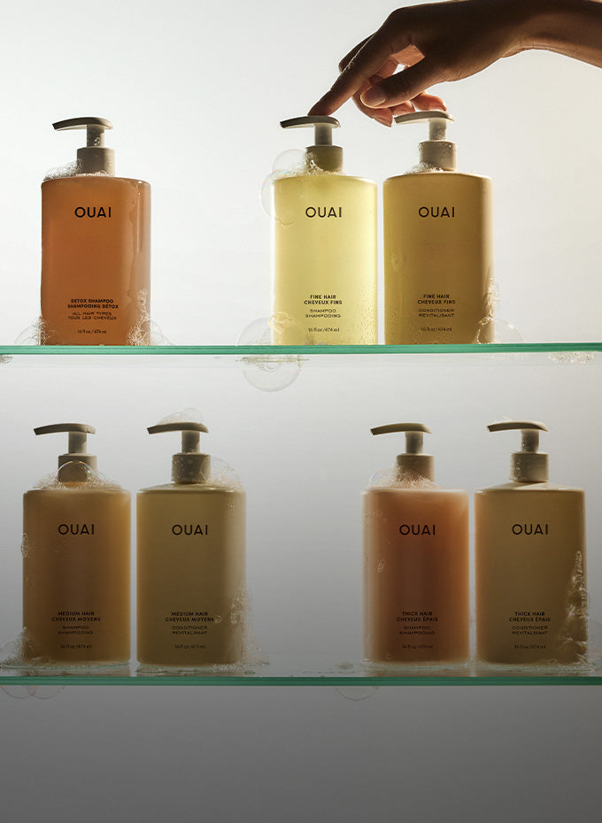 OUAI hair care products on a shelf with a hand reaching for one.