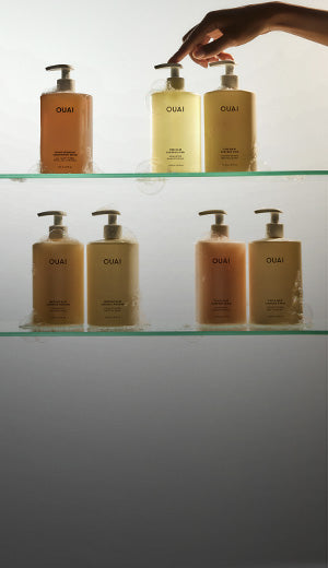 Hand reaching for a bottle of OUAI hair products on a glass shelf.