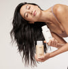 Woman holding OUAI hair care products against a neutral background