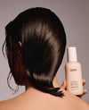 Person holding OUAI hair product with styled hair against a neutral background