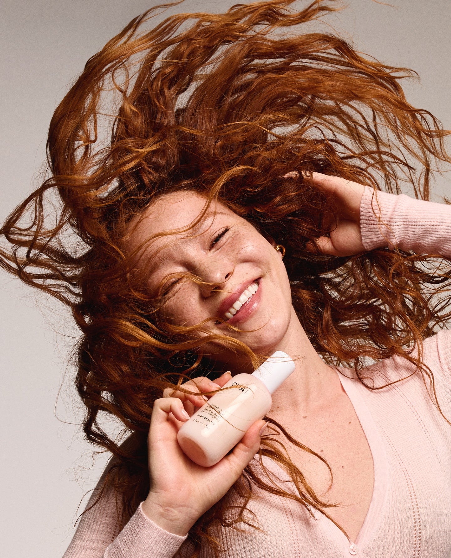 Woman with flowing red hair holding a bottle of shampoo against a neutral background