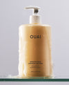 OUAI Medium Hair Shampoo 16oz bottle covered in lather on glass shelf.