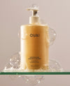 OUAI Medium Hair Shampoo bottle surrounded by bubbles on a glass shelf.