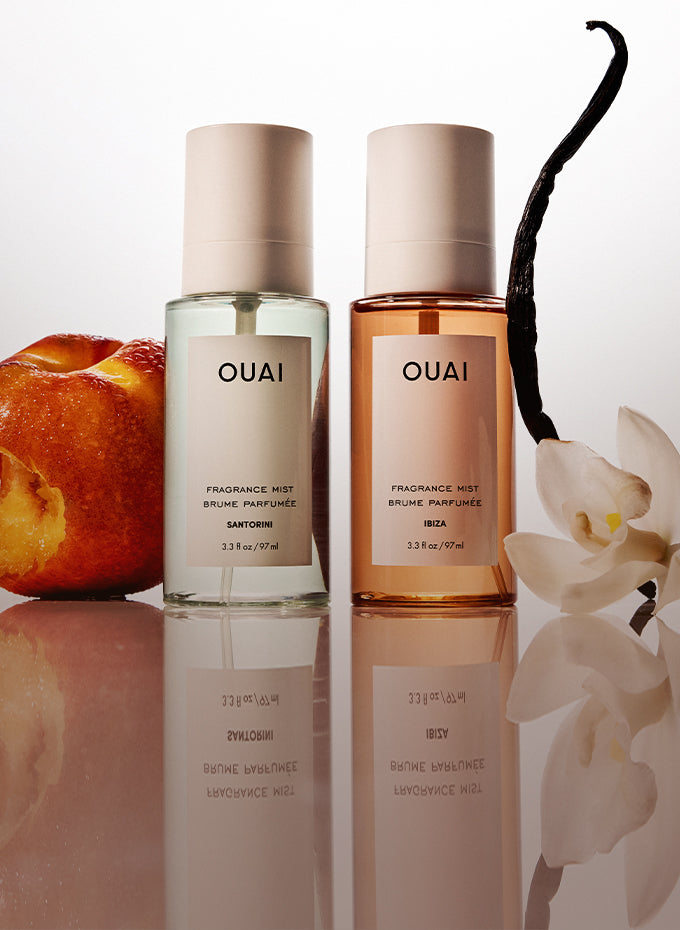 Two OUAI fragrance mists with a vanilla bean, peach, and orchid on a reflective surface.