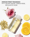 Ouai fine hair shampoo bottle styled with a pink rose, lemon slices, and jasmine flowers on a white background, with text reading 'MERCER STREET FRAGRANCE Notes of: ITALIAN LEMON, TURKISH ROSE, IRIS & WHITE MUSK'.