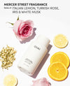 OUAI Medium Shampoo bottle on a white background, styled with a pink rose, lemon slices, jasmine blossoms, and text reading 'MERCER STREET FRAGRANCE Notes of: ITALIAN LEMON, TURKISH ROSE, IRIS & WHITE MUSK'.