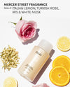 OUAI Medium Shampoo bottle on a white background, styled with a pink rose, lemon slices, jasmine blossoms, and text reading 'MERCER STREET FRAGRANCE Notes of: ITALIAN LEMON, TURKISH ROSE, IRIS & WHITE MUSK'.