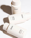 Three OUAI hair conditioner bottles arranged diagonally on a white background with soft shadows. The bottles are a warm off-white/cream color with black text, showing the OUAI brand name 
