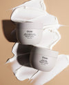 Two OUAI skincare cream jars arranged on a beige background with white cream swatches behind them. The top jar reads 'OUAI Fine to Medium AHA Cheveux Fine & Modifying Treatment Cream' and the bottom jar reads 'OUAI Thick AHA Exfoliating Treatment Cream.
