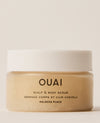 A translucent OUAI Melrose Place Scalp & Body Scrub jar filled with beige granules sits beneath a white lid against a warm cream backdrop.