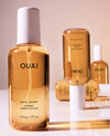 OUAI Wave Spray in an amber glass bottle with a white cap, shown alongside two additional bottles in a softly lit studio setting.