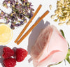 Herbs, cinnamon sticks, lemon, raspberries, and a pink rose on a white background